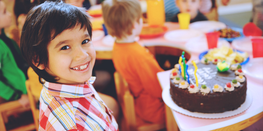 Un enfant très souriant qui fête son anniversaire avec un très beau gâteau au chocolat dans la plaine de jeu couverte