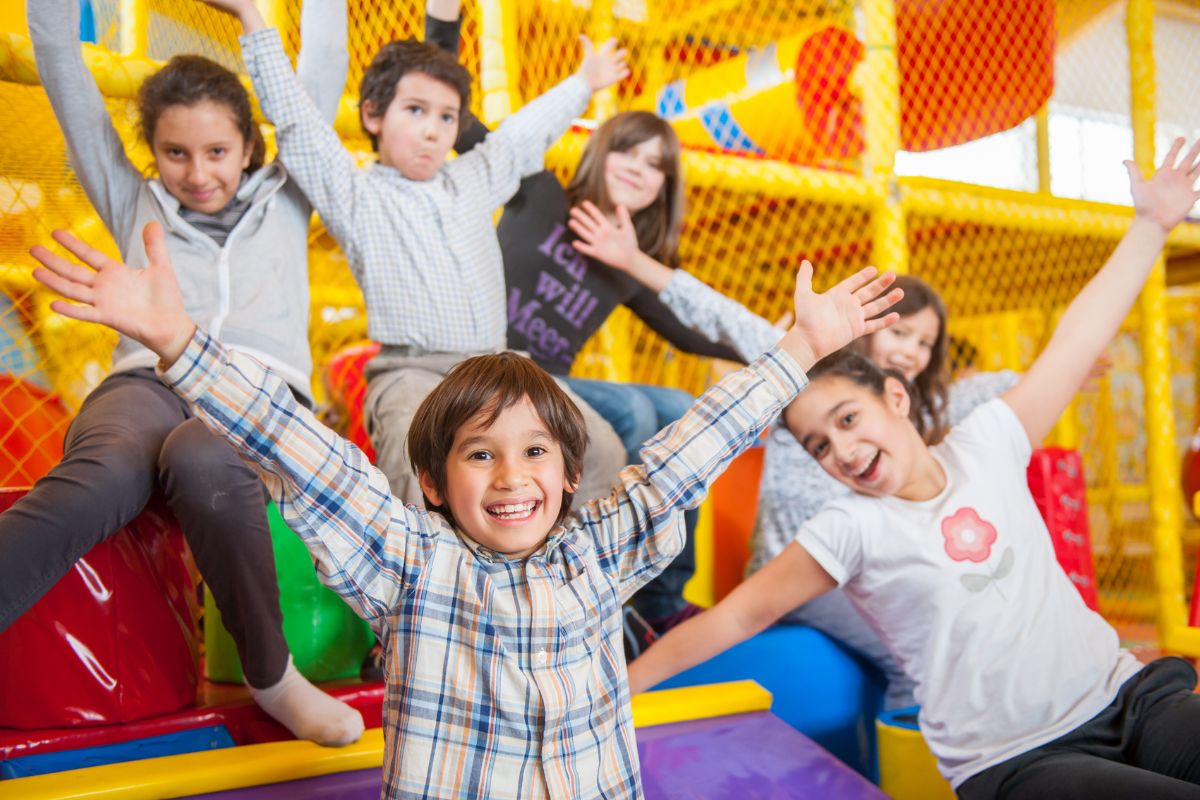 Des enfants souriants qui lèvent les bras dans la plaine de jeux couverte